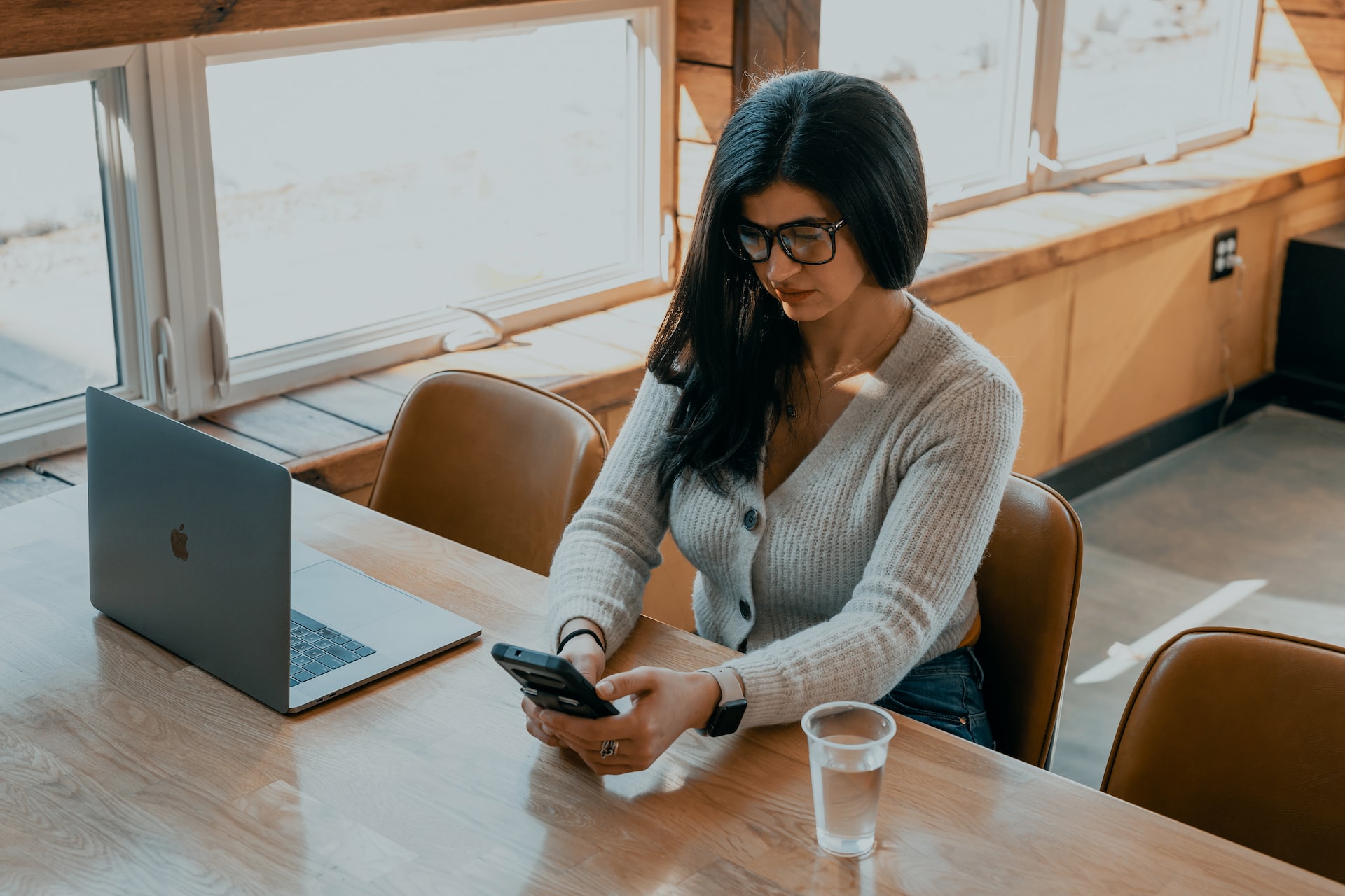 woman in white sweater sitting on chair holding smartphone